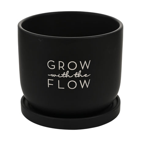 Round ceramic planter in matt black with "Grow with the Flow" white printed text, shown with a matching black saucer on a plain white background.