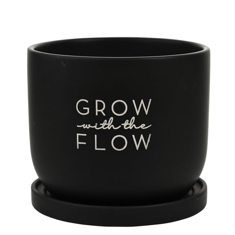 Round ceramic planter in matt black with "Grow with the Flow" printed in white lettering, shown on a matching black saucer against a plain white background.