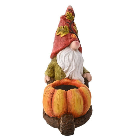 Rear view of the ceramic gonk garden ornament in a red leaf-patterned hat, white beard, and olive jacket, pushing an orange pumpkin wheelbarrow planter on a plain white background.
