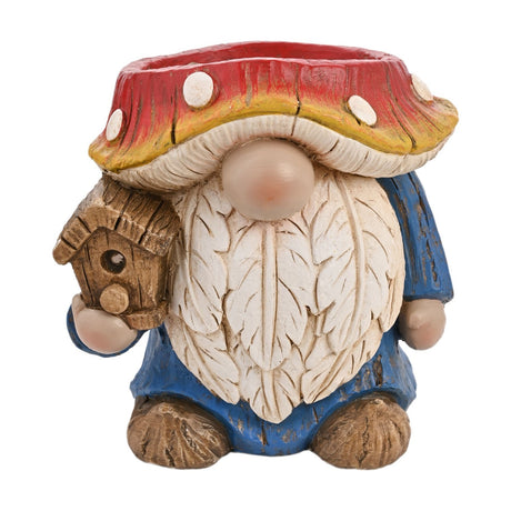 Ceramic gnome planter with a red-and-yellow spotted mushroom hat as the pot, cream leaf-textured beard, blue robe, brown boots, and a wooden birdhouse at its side.