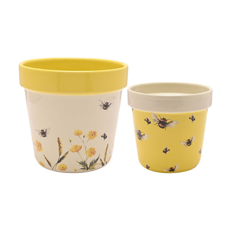 Set of 2 round ceramic flowerpot planters, the larger cream with a yellow rim and wildflower and bee design, the smaller yellow with a cream rim and bumblebee print, on a white background.