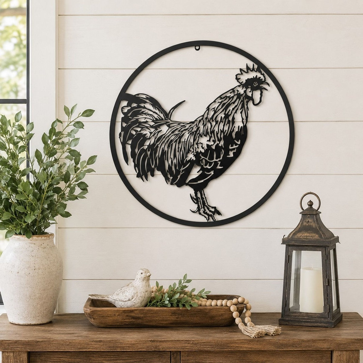 Round Cockerel Metal Wall Art, black 60cm cut-out design in a slim circular frame, shown mounted on a shiplap wall above a wooden console table with decor.