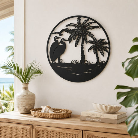 Round Wild Birds and Palm Trees Metal Wall Art, 40cm, black silhouette design with two wading birds and palm trees, shown mounted on a light wall above a wooden sideboard.