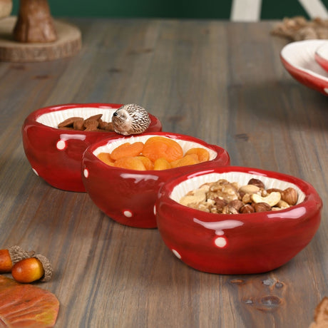 Glossy red toadstool-and-hedgehog triple dish serving tray with white spots, cream ribbed bowls, and a modelled hedgehog on the rim, filled with nuts and dried fruit.