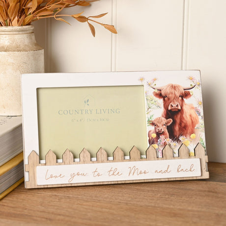 Wooden 6"x4" photo frame with Highland cow and calf among wildflowers, picket fence base, and "Love you to the Moo and back" script, displayed beside a vase and books.