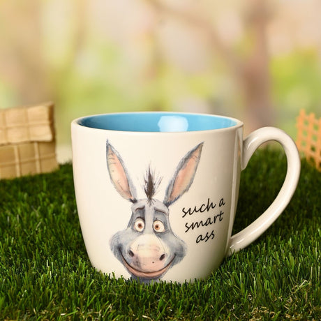 Cream earthenware mug with blue interior, featuring a grey watercolour donkey face and "such a smart ass" script, shown outdoors on grass.