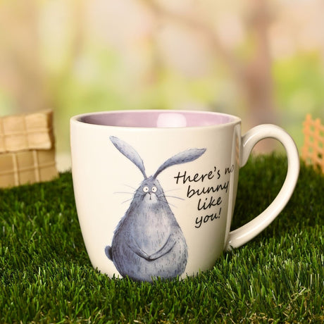 White earthenware mug with pink interior, featuring a hand-drawn grey rabbit and "there's no bunny like you" script, shown outdoors on grass.