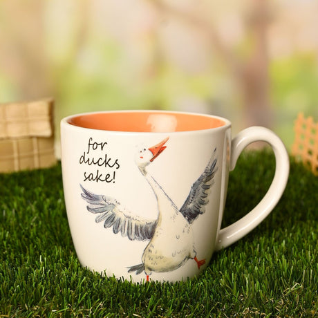 White earthenware mug with orange interior, featuring a hand-drawn flapping goose and "for ducks sake!" script, shown outdoors on grass with a C-shaped handle.