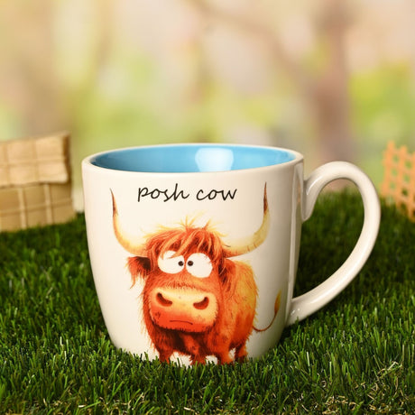 White earthenware "Posh Cow" mug with blue interior, featuring an illustrated Highland cow and "posh cow" script, set on grass outdoors.
