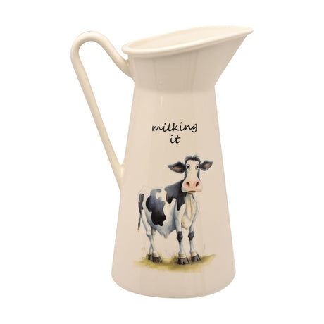 White ceramic milk jug vase with curved handle, featuring a painted black and white cow and "milking it" script, shown on a plain white background.