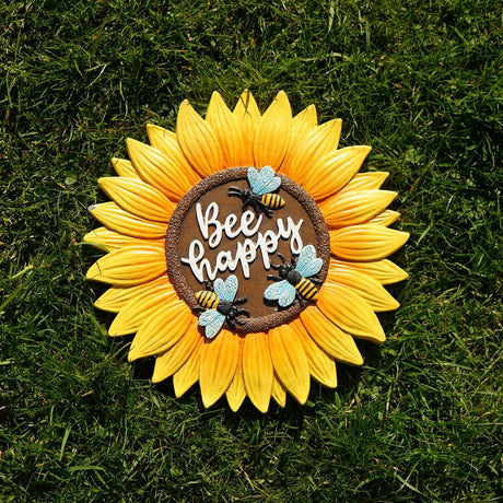 Bee Happy Sunflower Resin Stepping Stone in yellow and brown, round with pointed petals, textured centre, raised lettering and three bees, shown on grass.