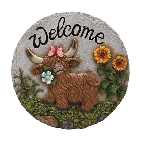 Round resin stepping stone with "Welcome" text above a raised Highland cow, pink butterfly, flower, and sunflowers on a grey stone-textured ground.