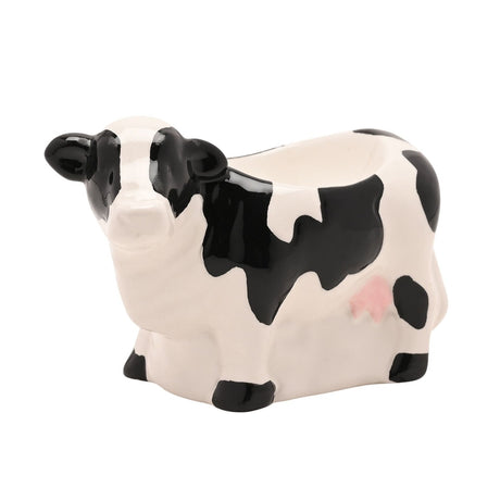 Standing Cow Earthenware Egg Cup in white with black patches, black hooves and ears, and a pink udder, cup hollow on its back, shown on a plain white background.