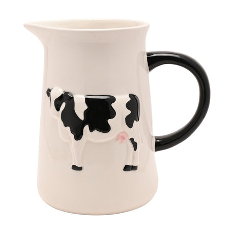 Cream earthenware jug with a raised black-and-white cow design in relief, black curved handle, and pouring spout, shown on a plain white background.