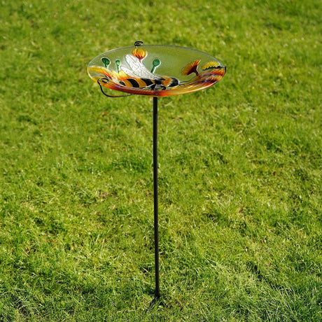 Round glass bird feeder on a metal garden stake, 30.5cm dish featuring a yellow and black bee among orange and yellow flowers on clear glass, set in grass.