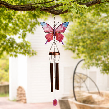 Butterfly Solar Iron & Glass Wind Chime in pink and copper, with glass wings, copper tubes, and a hanging petal charm, shown outdoors beneath leafy branches.