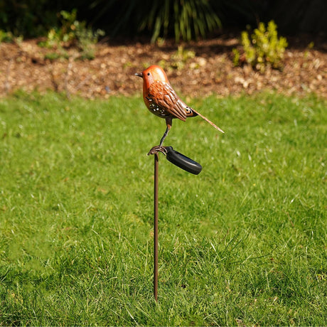 Robin Solar Stake garden ornament in brown and orange plastic, perched on a slim stake with a solar unit, shown standing in grass in a garden setting.