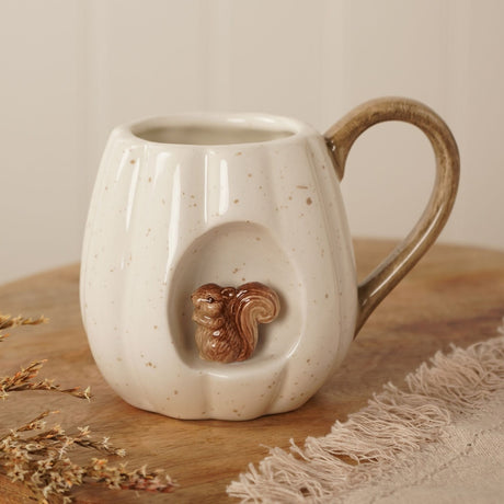 Speckled Pumpkin Squirrel Insert Ceramic Mug 320ml in cream, with ribbed pumpkin-shaped body, a sculpted squirrel in a front recess, and a streaked brown curved handle, shown on a wood surface.