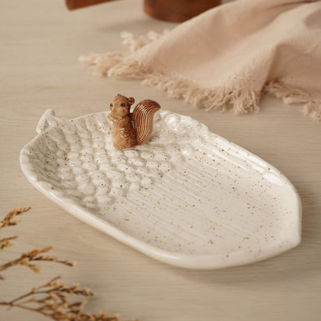 Speckled Acorn Ceramic Plate with Sculpted Squirrel in cream, shaped like an acorn with textured cup detailing and ribbed centre, shown on a wooden surface with linen and dried florals.