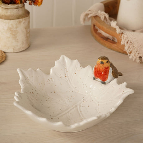 Large speckled cream ceramic leaf-shaped plate with raised vein detail and a perched robin figure in orange, brown and white, shown on a wooden surface.