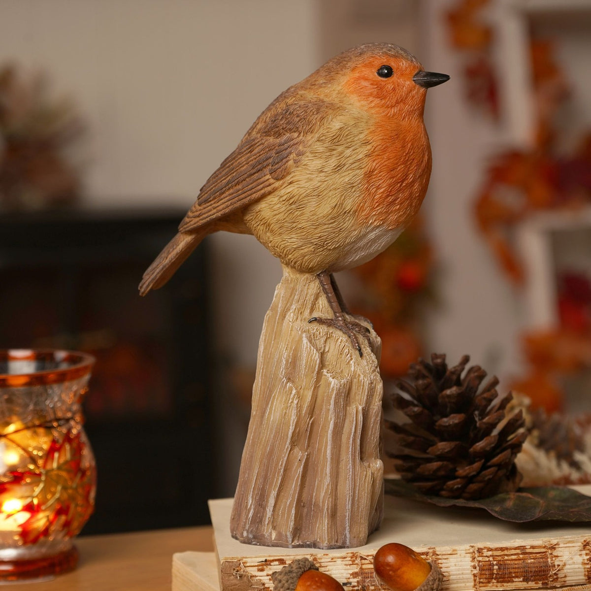 Robin Perched on a Trunk Resin Figurine in brown and orange, with textured feather detail and cream belly, displayed on a tree-stump base beside pine cones and a lit candle holder.