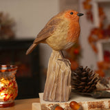 Robin Perched on a Trunk Resin Figurine in brown and orange, with textured feather detail and cream belly, displayed on a tree-stump base beside pine cones and a lit candle holder.