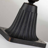 A close-up of the Cleveland Small Pedestal Lantern's fluted, dark metal base reveals a rectangular mounting plate. The weathered bronze finish displays a speckled texture with subtle hints of wear and age against a soft gray background.