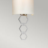 The Clark Small Wall Light - Polished Chrome features a contemporary light fixture with a faux silk cylindrical white shade, embellished with three polished chrome hexagon rings hanging from its base, all set against a plain gray background.