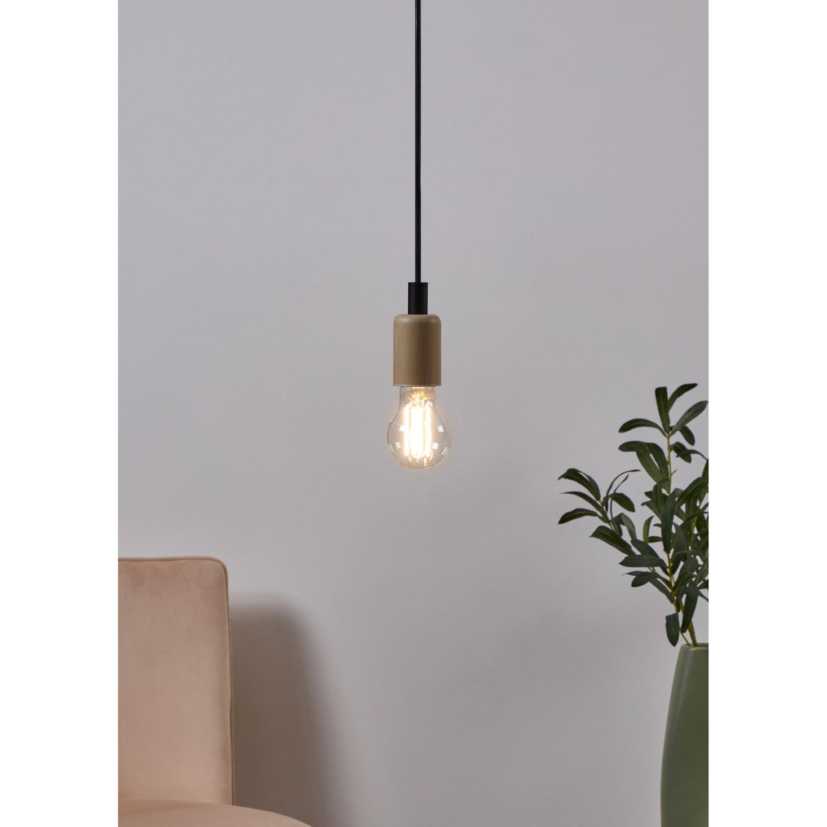 Clear LED GLS bulb with visible filaments, E27 cap, hanging lit from a black pendant cord against a light grey wall in a living room setting.