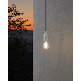 Clear GLS LED bulb with E27 cap glowing warm white, shown lit in a minimalist pendant fitting against a textured wall at dusk.