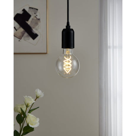 Clear LED globe bulb, E27 fitting, with visible spiral filament glowing warm white, shown in a black pendant fitting against a neutral room setting.