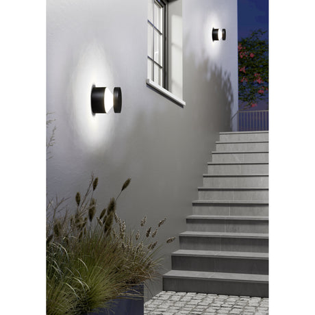 Clerbora LED Outdoor Wall Light in black cylindrical aluminium, mounted beside a staircase and window, casting warm white uplight and downlight on an exterior wall at night.