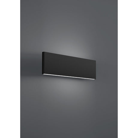 Climene LED Wall Light in black, a slim rectangular aluminium fixture mounted on a dark grey wall, with a white diffuser strip casting warm upward and downward light.