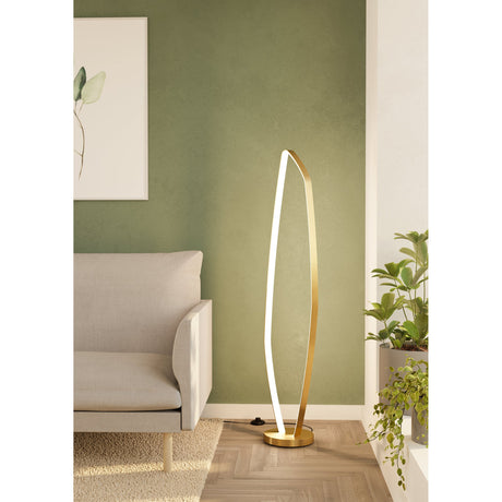 Clomelle LED Floor Lamp in brushed brass, a tall open leaf-shaped loop on a round disc base, shown beside a sofa and plants in a living room.