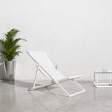 Club Aluminium Folding Deck Chair in white, reclined sling seat on an aluminium frame, shown beside a potted palm and glass side table on a light concrete floor.