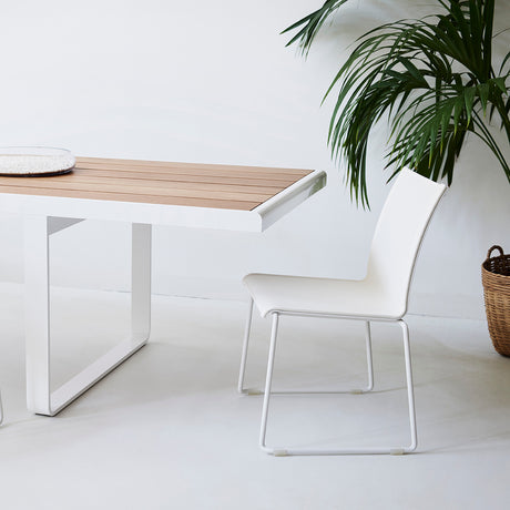 Club Aluminium Stacking Garden Chair with white sled base and white Vinytex seat, shown beside a wood-top dining table in a light interior setting.