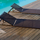 Two Club aluminium sun loungers with dark mesh sling seats and bronze-toned frames, adjustable backrests raised, positioned on a wooden deck beside a pool.