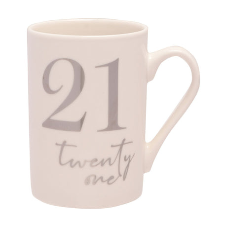 White ceramic 21st birthday mug with silver foil "21" and "twenty one" script, curved handle, tall straight sides, on a plain white background.