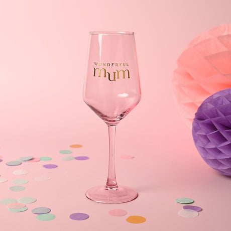 Pink stemmed wine glass with tapering bowl, featuring "WONDERFUL mum" in gold lettering, set against a pink background with confetti and honeycomb decorations.