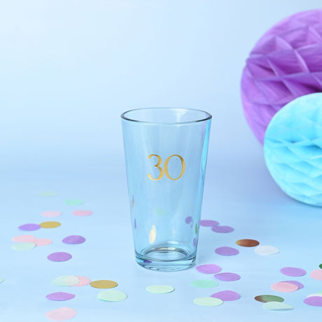 Tapered beer glass in pale blue-tinted glass with "30" in gold foil, pictured with pastel confetti and purple and blue honeycomb decorations.