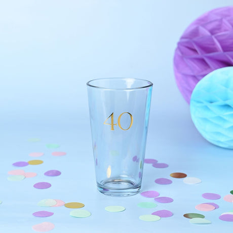 Clear tapered beer glass with gold foil "40" in serif font, set on a light blue background with pastel confetti and honeycomb decorations.