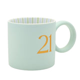 Light blue matt porcelain mug with round ring handle, featuring a gold serif "21" on the side and green and blue striped interior, shown on a white background.