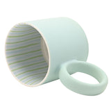 Matt porcelain mug in pale light blue with a round ring handle, tipped on its side to show the interior lined with thin green and pale blue stripes, on a plain white background.