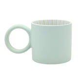 Matt porcelain mug with a round ring handle in pale light blue, showing green and blue striped interior, on a plain white background.