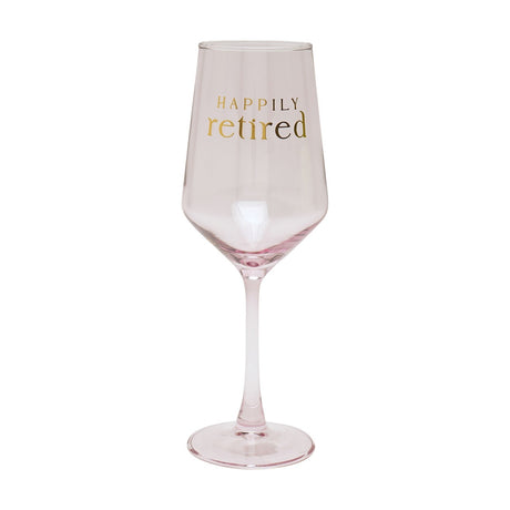 Pale pink wine glass with a slim stem and round foot, featuring gold foil "HAPPILY retired" lettering on the bowl, shown against a plain white background.