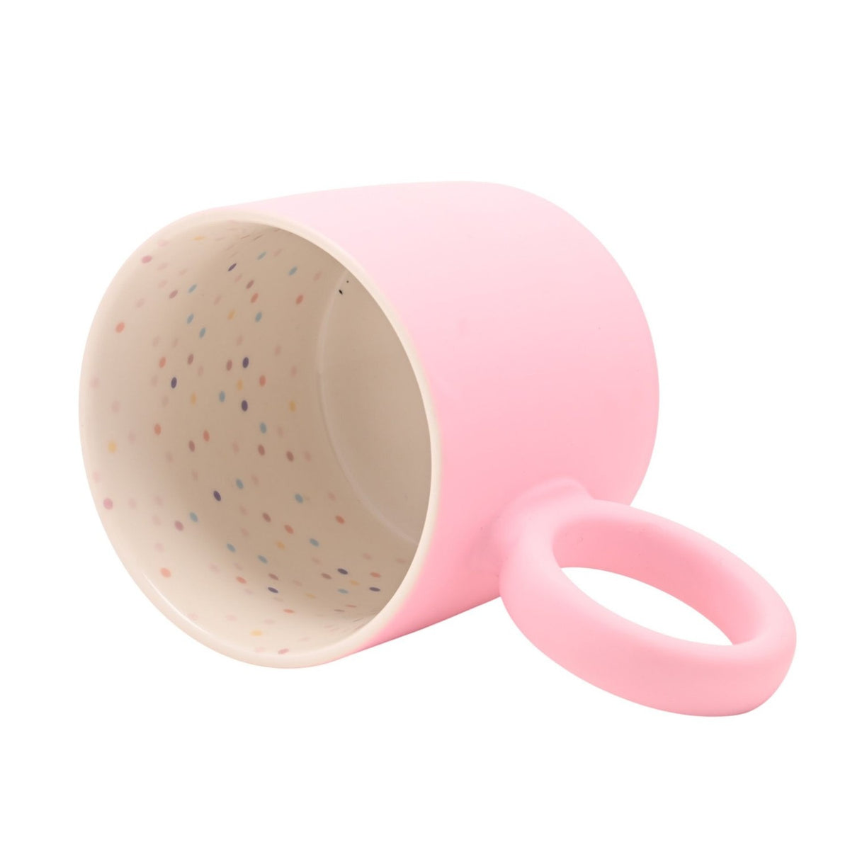 Matt pink porcelain mug tipped on its side showing a chunky round handle and cream interior speckled with multicoloured dots, on a plain white background.