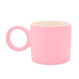 Matt porcelain mug in soft pink with a chunky round ring handle, smooth matt exterior, and a creamy white interior speckled with pink, peach, blue and grey dots, shown on a plain white background.