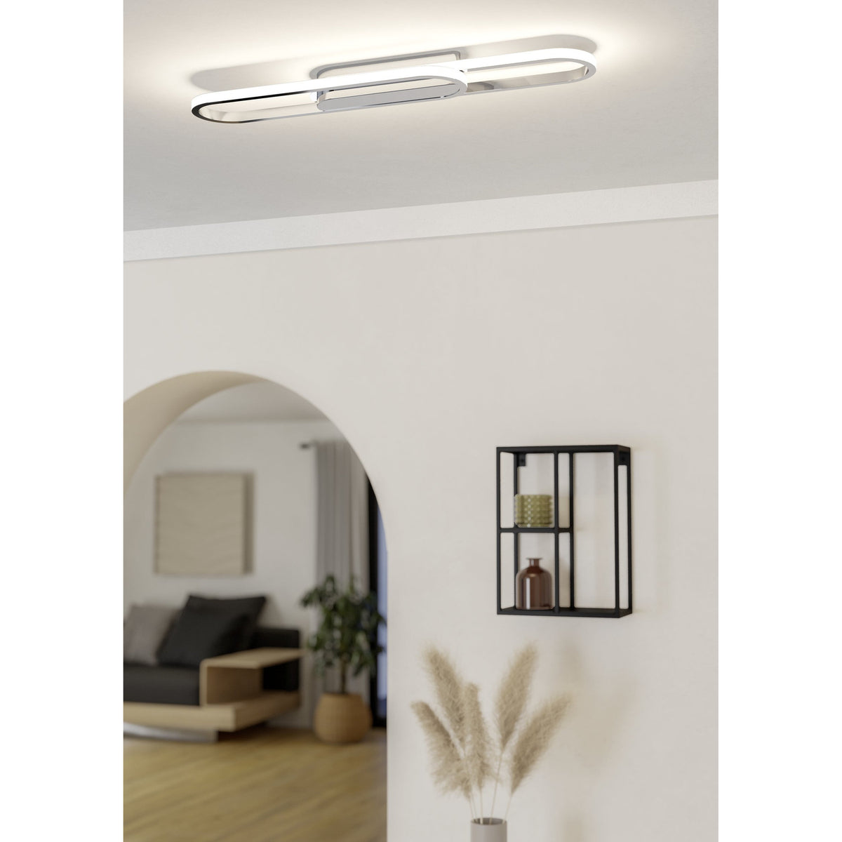Conivarena LED flush ceiling light in chrome, an elongated oblong loop with a central chrome bar, mounted on a hallway ceiling with white walls and an arched doorway.
