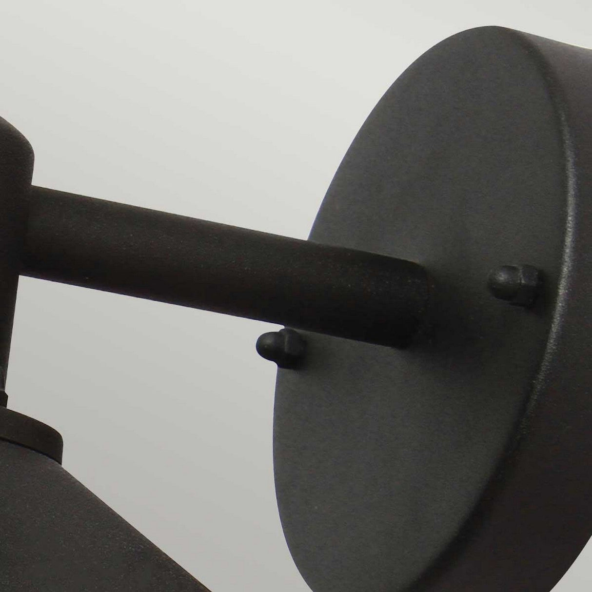 Close-up of a minimalist Copenhagen Outdoor Wall Lantern - Black. The round backplate and cylindrical arm, crafted in stainless steel, stand out against a light gray background. Its sleek design is complemented by an IP44 rating, ensuring durability for any modern space.