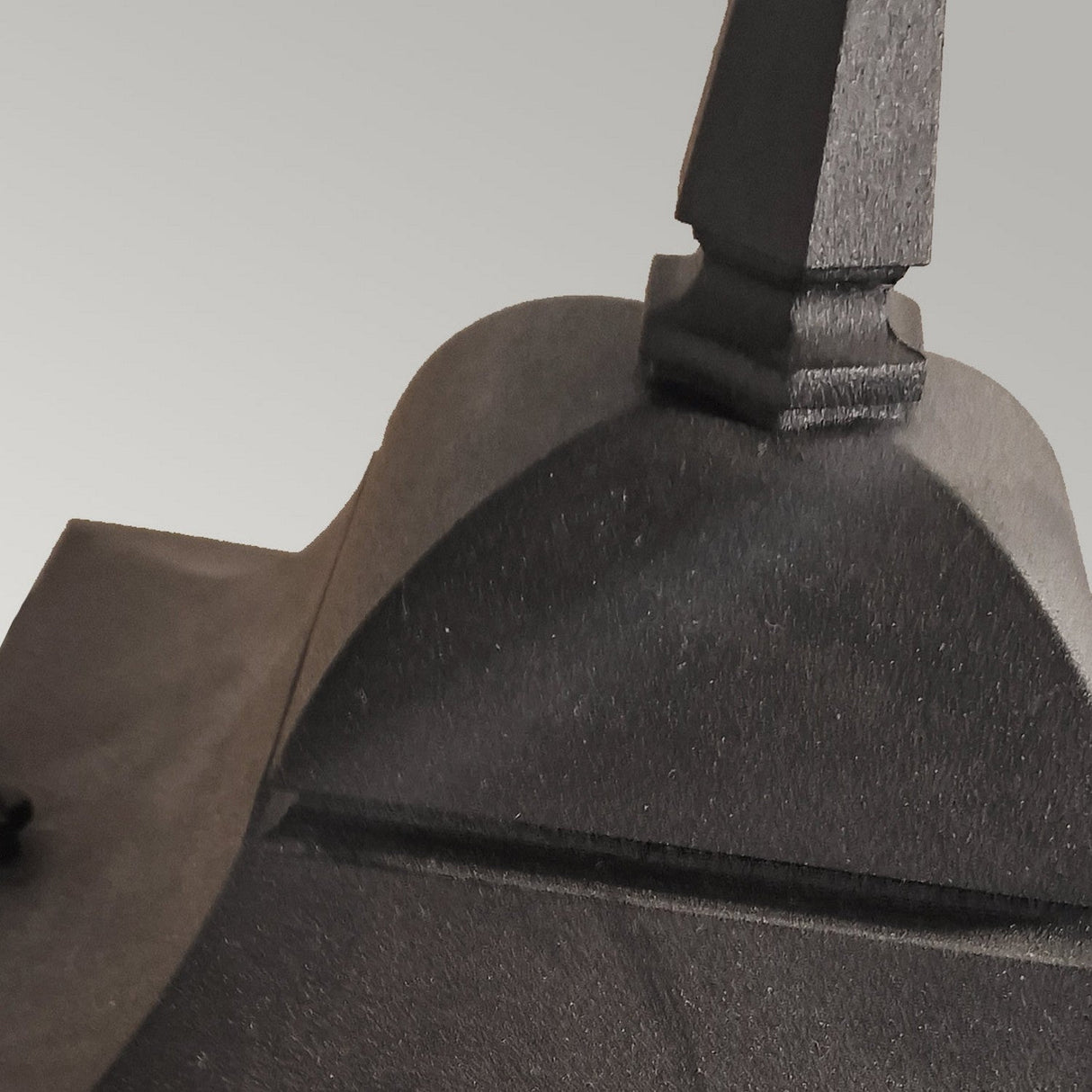 Close-up of the Chapel 1 Light Outdoor Up Wall Lantern in black, featuring an intricate, curved design with a pointed tip, crafted from die-cast aluminium. The lighting accentuates the texture and contours of its surface against a plain background.